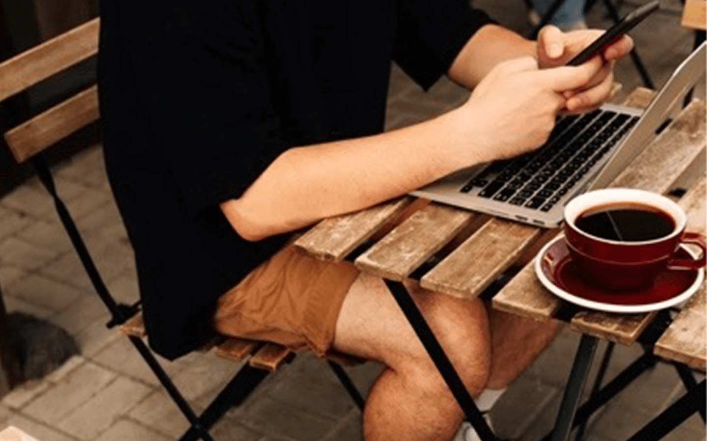 Young man sitting at his laptop while using his phone with a cup of coffee (an anxiety inducing stimulant) placed nearby