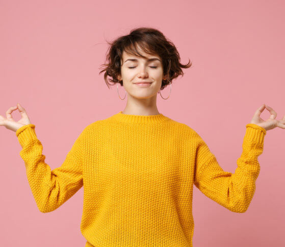 Young brunette woman girl in yellow sweater posing isolated on pastel pink background. People lifestyle concept. Mock up copy space. Hold hands in yoga gesture relaxing meditating keeping eyes closed