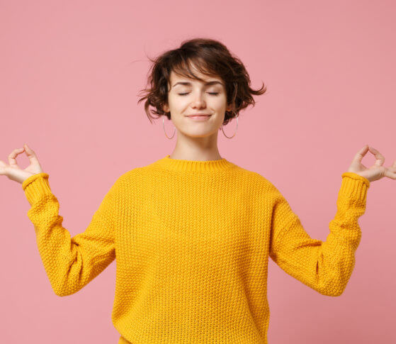 Young brunette woman girl in yellow sweater posing isolated on pastel pink background. People lifestyle concept. Mock up copy space. Hold hands in yoga gesture relaxing meditating keeping eyes closed